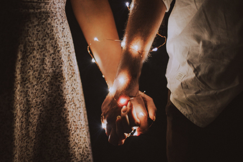 Close up image of two people holding hands with fairy lights wrapped around them
